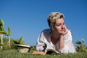 femme allongée et lisant son livre préféré sur un pré recouvert d'herbe verte fraîche par un été ensoleillé ou une journée de printemps. photo