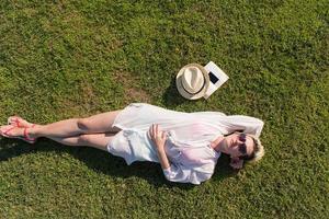 Haut vue de au dessus de une femme mensonge et relaxant sur une Prairie couvert avec vert herbe sur une ensoleillé été ou printemps journée. photo