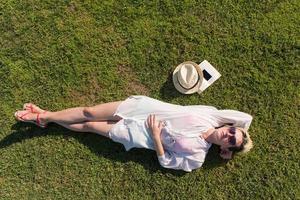 Haut vue de au dessus de une femme mensonge et relaxant sur une Prairie couvert avec vert herbe sur une ensoleillé été ou printemps journée. photo