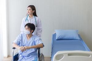 femme médecin asiatique parlant avec un patient homme qui porte un masque facial sur ses symptômes de santé alors qu'il est assis sur un fauteuil roulant à l'hôpital. photo