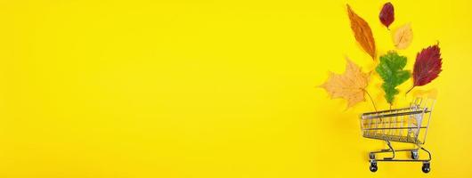 concept de vente d'automne. panier et feuilles colorées tombées sur fond jaune. composition créative pour la publicité. photo