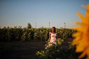 jolie jeune femme noire porte une robe d'été pose dans un champ de tournesol. photo