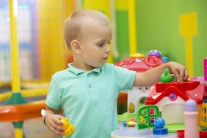 une peu garçon pièces avec une lot de coloré Plastique jouets à l'intérieur. photo