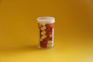 rouge et blanc médical pilules tablette capsule à l'intérieur petit clair récipient avec papier étiquettes isolé sur Jaune Contexte. photo
