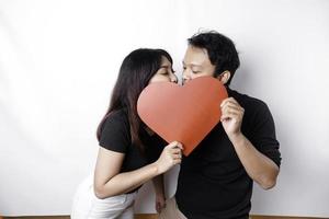 une couple dans l'amour détient une papier rouge cœur, couvrant leur visages. content la Saint-Valentin journée photo