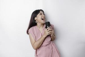 portrait d'une femme asiatique insouciante, s'amusant au karaoké, chantant au microphone en se tenant debout sur fond blanc photo