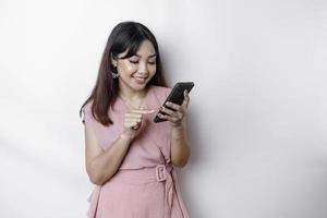 une portrait de une content asiatique femme habillé dans rose et en portant sa téléphone, isolé par blanc Contexte photo