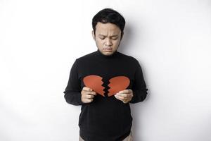 magnifique Jeune asiatique homme exprimé le sien tristesse tandis que en portant cassé cœur isolé sur blanc Contexte photo