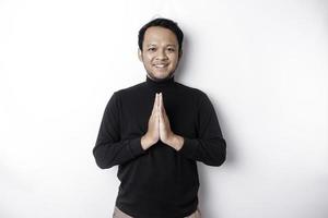 souriant Jeune asiatique homme portant noir chemise, faire des gestes traditionnel salutation isolé plus de blanc Contexte photo