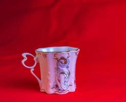 porcelaine rose tasse de un inhabituel forme est fabriqué dans le tchèque république. une tasse avec une romantique modèle sur une rouge Contexte. photo