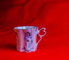 porcelaine rose tasse de un inhabituel forme est fabriqué dans le tchèque république. une tasse avec une romantique modèle sur une rouge Contexte. photo