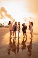 une groupe de asiatique femmes dans chemises posant Heureusement tandis que visite une magnifique plage photo