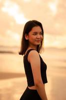 une magnifique asiatique femme dans noir vêtements est profiter le beauté de le plage avec une souriant expression sur sa visage tandis que sur vacances photo
