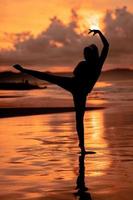 une balinais femme dans le forme de une silhouette effectue ballet mouvements très habilement et avec souplesse sur le plage avec le vagues s'écraser photo