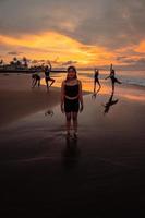 portrait de un asiatique femme dans noir vêtements permanent sur le plage avec sa copains dansant derrière sa photo