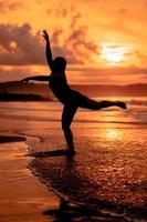silhouette de un asiatique femme dansant ballet avec génial souplesse et une vue de le vagues derrière sa photo
