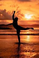 silhouette de un asiatique femme dansant ballet avec génial souplesse et une vue de le vagues derrière sa photo