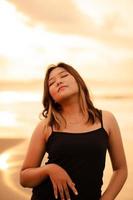 une blond asiatique femme avec une magnifique visage et noir vêtements profiter le beauté de le plage et le vagues dans le Matin photo