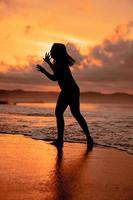 un asiatique femme dans le forme de une silhouette Faire ballet mouvements très agile sur le plage photo