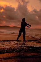 un asiatique femme qui est en jouant et dansant sur le plage avec fort vagues photo