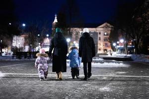 retour de famille marcher par le nuit ville dans le l'hiver. mère et Trois les enfants dans soir. photo