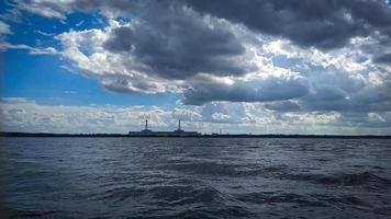 bleu ciel plus de ondulé Lac paysage, la nature Contexte avec lourd des nuages au dessus et visible visaginas nucléaire Puissance plante sur le Contexte photo