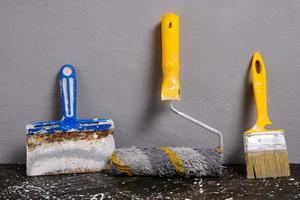 peindre rouleau, brosse et spatule sur une gris mur arrière-plan, réparation outil. photo