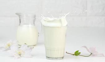 plein verre tasse de Frais Lait avec éclaboussures des stands sur une blanc tableau, en bonne santé petit déjeuner photo