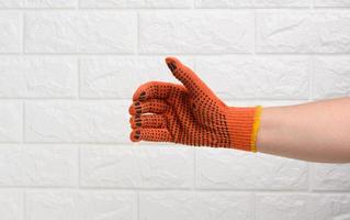 femelle main dans un Orange travail protecteur gant contre le Contexte de une blanc brique mur, le main conditionnellement détient un objet photo