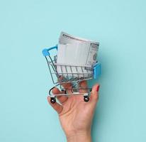 femelle mains tenir métal miniature chariot avec nous papier dollars sur une bleu Contexte. vente concept photo