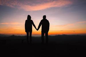 silhouette de une homme et femme en portant mains avec chaque autre avec une magnifique le coucher du soleil dans Contexte. content mode de vie concept. photo