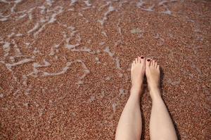 concept de voyage - jambes de femme sur une belle plage tropicale avec du sable de galets. les pieds sur le sable et les vagues en été. fille pieds nus dans l'eau de mer en voyage de vacances. se sentir heureux et se détendre. espace de copie. photo