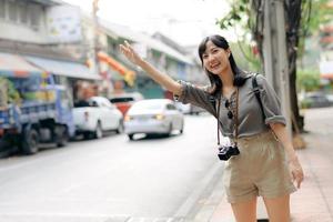 souriant Jeune asiatique femme voyageur auto-stop sur une route dans le ville. la vie est une périple concept. photo