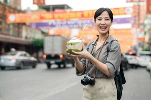 content Jeune asiatique femme sac à dos voyageur en buvant une noix de coco jus à Chine ville rue nourriture marché dans Bangkok, Thaïlande. voyageur vérification en dehors côté des rues. photo