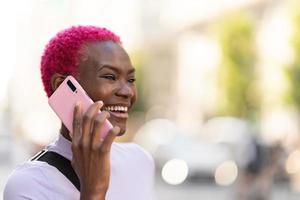 élégant africain femme souriant tandis que parlant à le mobile en plein air photo