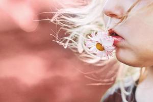 fille avec une Marguerite fleur sur une rose Contexte fermer. lèvres avec fleur sur une rose Contexte. portrait de une peu fille photo