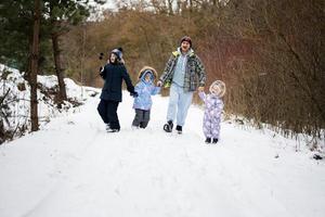 père avec Trois des gamins en portant mains et en marchant dans hiver forêt. photo
