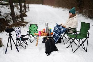 femme asseoir dans chaise et lis livre dans hiver forêt sur une pique-nique. photo