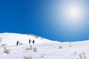 alpinistes escalade neigeux montagnes avec sacs à dos sur ensoleillé journée photo