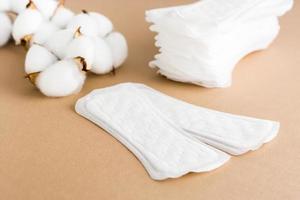 deux nettoyer jetable sanitaire tampons, une empiler de tampons et une branche de coton sur une beige Contexte. aux femmes santé et confort concept photo