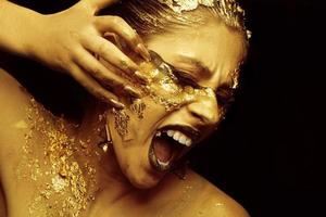 une magnifique fille déchire de sa visage avec d'or maquillage sur une noir Contexte. photo
