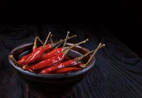 une argile tasse avec mariné le Chili poivrons des stands sur une foncé en bois Contexte. photo