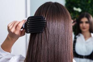 jeune femme peignant ses longs cheveux noirs avec un peigne dans un salon de beauté. une chevelure brune droite et saine qui a subi la procédure de lissage des cheveux. photo