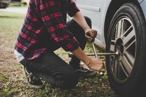 jeune femme hipster vérifiant un pneu crevé sur sa voiture photo