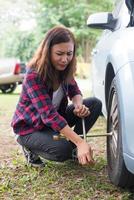 jeune femme hipster vérifiant un pneu crevé sur sa voiture