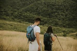 Couple souriant marchant avec des sacs à dos sur les collines verdoyantes photo