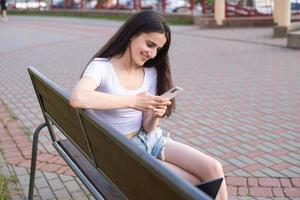 une mignonne fille est séance sur une banc et l'écriture une message sur le téléphone à une gars photo