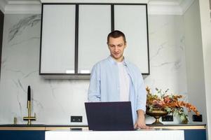 une Jeune homme dans une chemise travaux de Accueil sur une portable tandis que permanent dans le cuisine photo