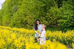 une mignonne garçon dans une blanc T-shirt donne le sien mère Jaune fleurs photo