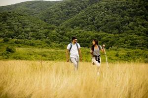 Couple souriant marchant avec des sacs à dos sur les collines verdoyantes photo